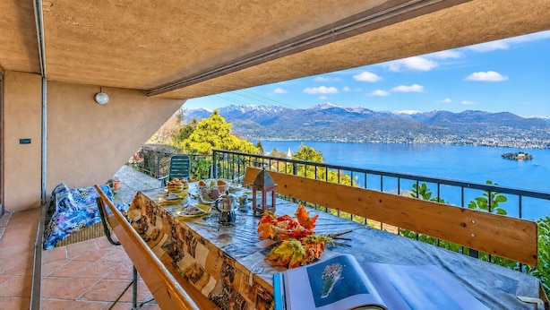 A balcony with a table set for dining, overlooking a lake and mountains. - Isola Bella: Lake Maggiore View Terrace in Stresa (Stresa)