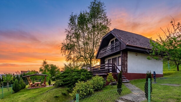 A rustic wooden house with a sloped roof, surrounded by a well-maintained lawn and a swing set. - Karesz Holiday Home /w Terrace & Garden (Zalakaros)