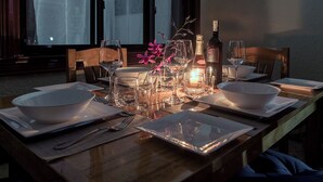 Una mesa de comedor dispuesta con cuencos blancos, copas de vino y una botella de champán, con una vela y flores sobre la mesa.