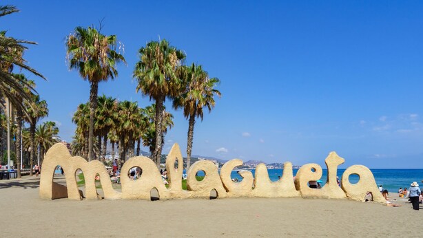 Een strand met een groot zandsculptuur dat 'Malagueta' spelt.