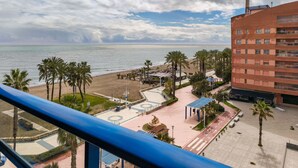 Een kustgezicht met een strand, palmbomen en een gebouw met een bakstenen gevel.