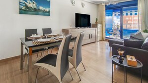 Een moderne woonkamer met een eethoek, een flatscreen televisie en een groot raam met uitzicht op gebouwen.