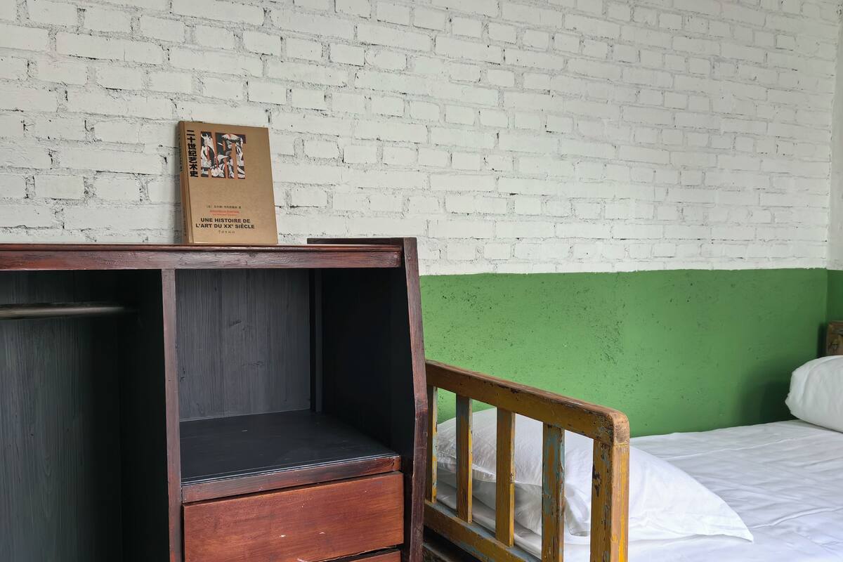 Une pièce avec une commode en bois, un mur vert et un lit blanc.