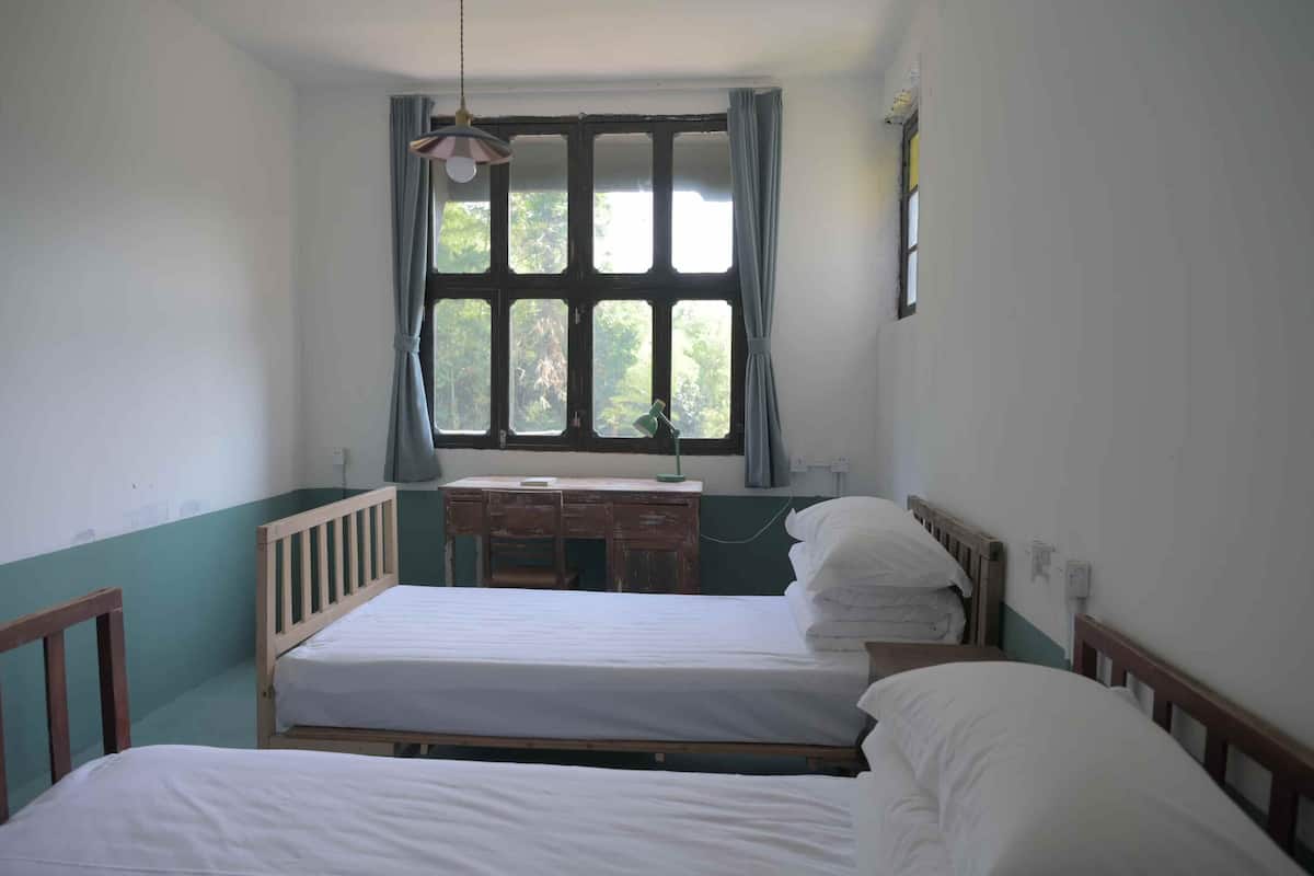 Une chambre avec deux lits en bois, un bureau et une fenêtre avec des rideaux.