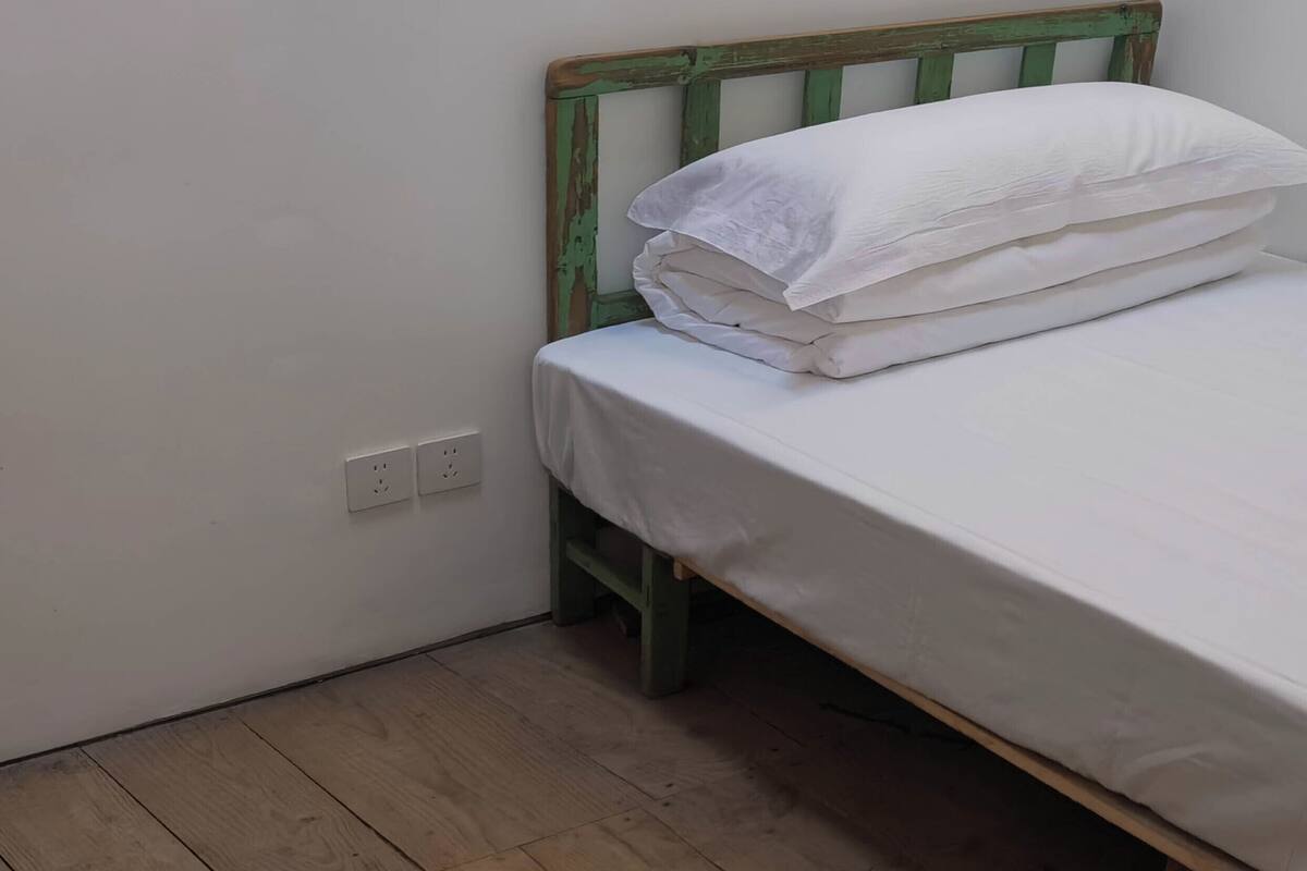 Une petite chambre avec un lit simple, un cadre en bois et du linge de lit blanc.