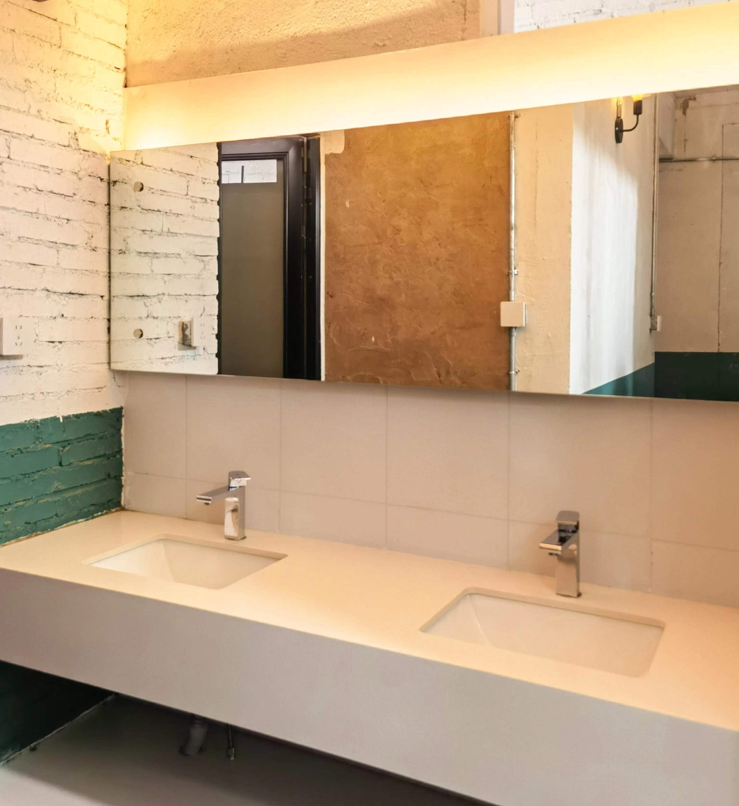 Un baño con dos lavamanos, un espejo y una lámpara sobre el espejo.