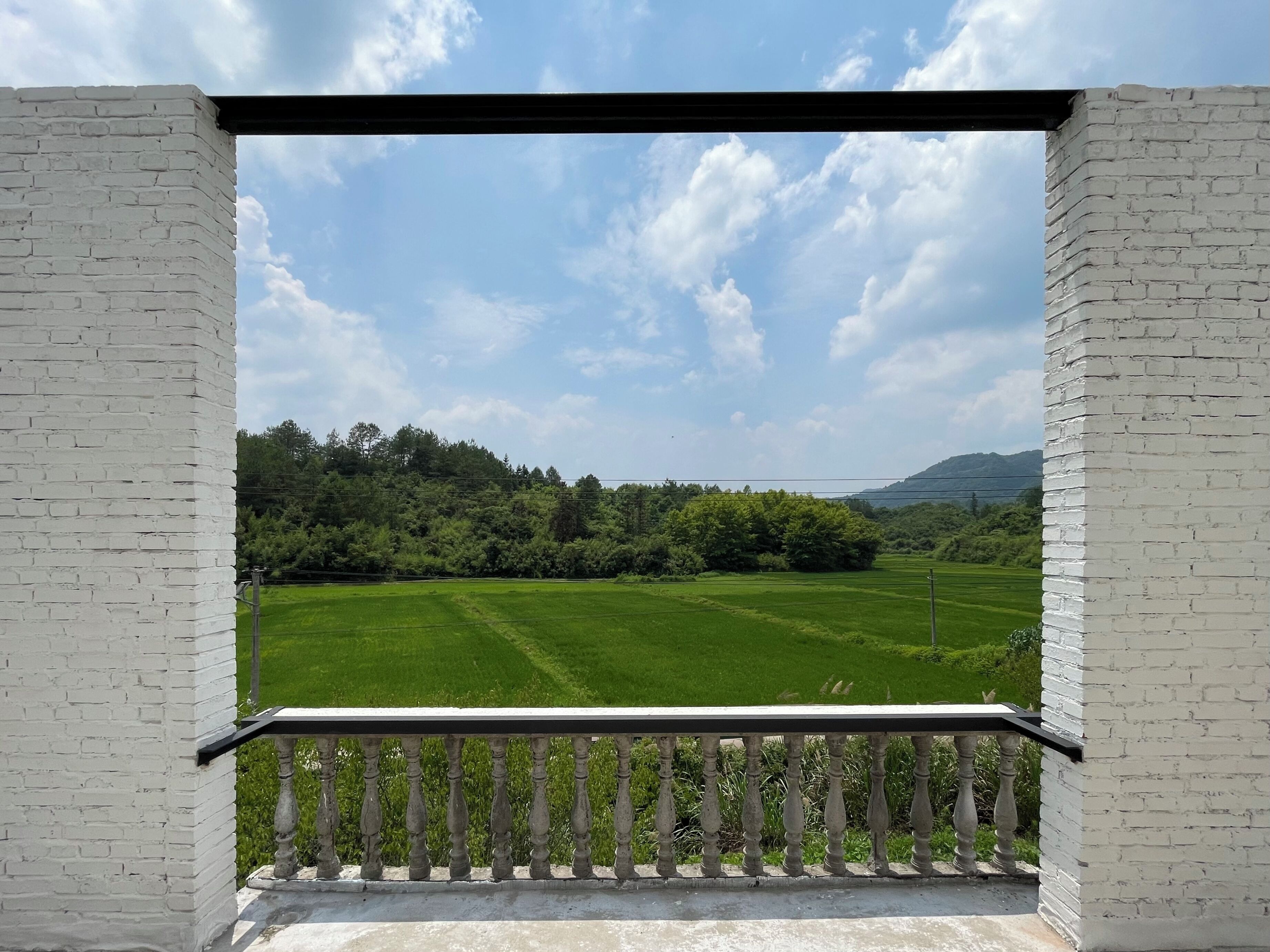 Un balcon donnant sur un champ verdoyant et des arbres, sous un ciel dégagé.