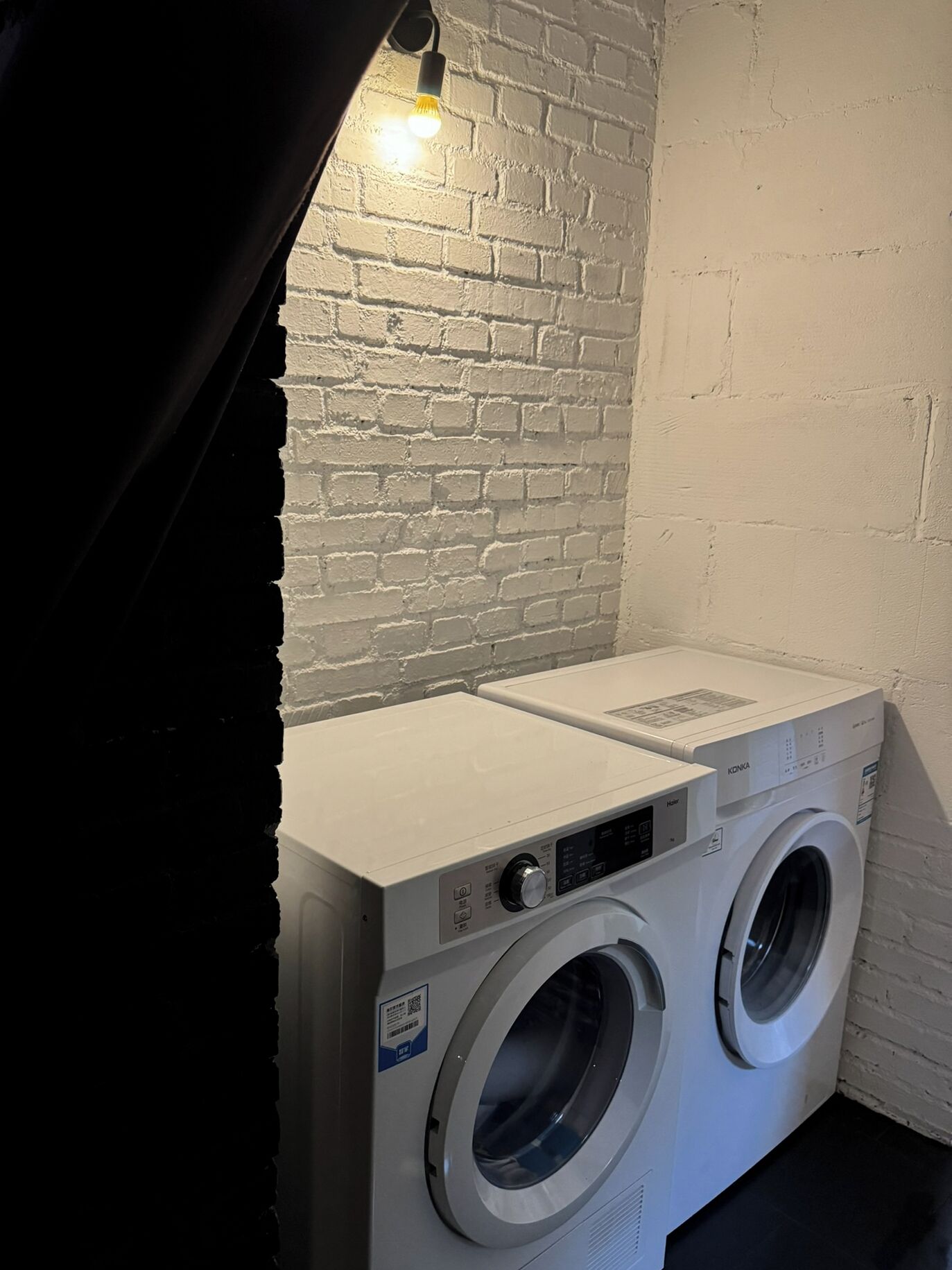 Een wasserette met twee voorladers, een witte bakstenen muur en een lamp boven de machines.