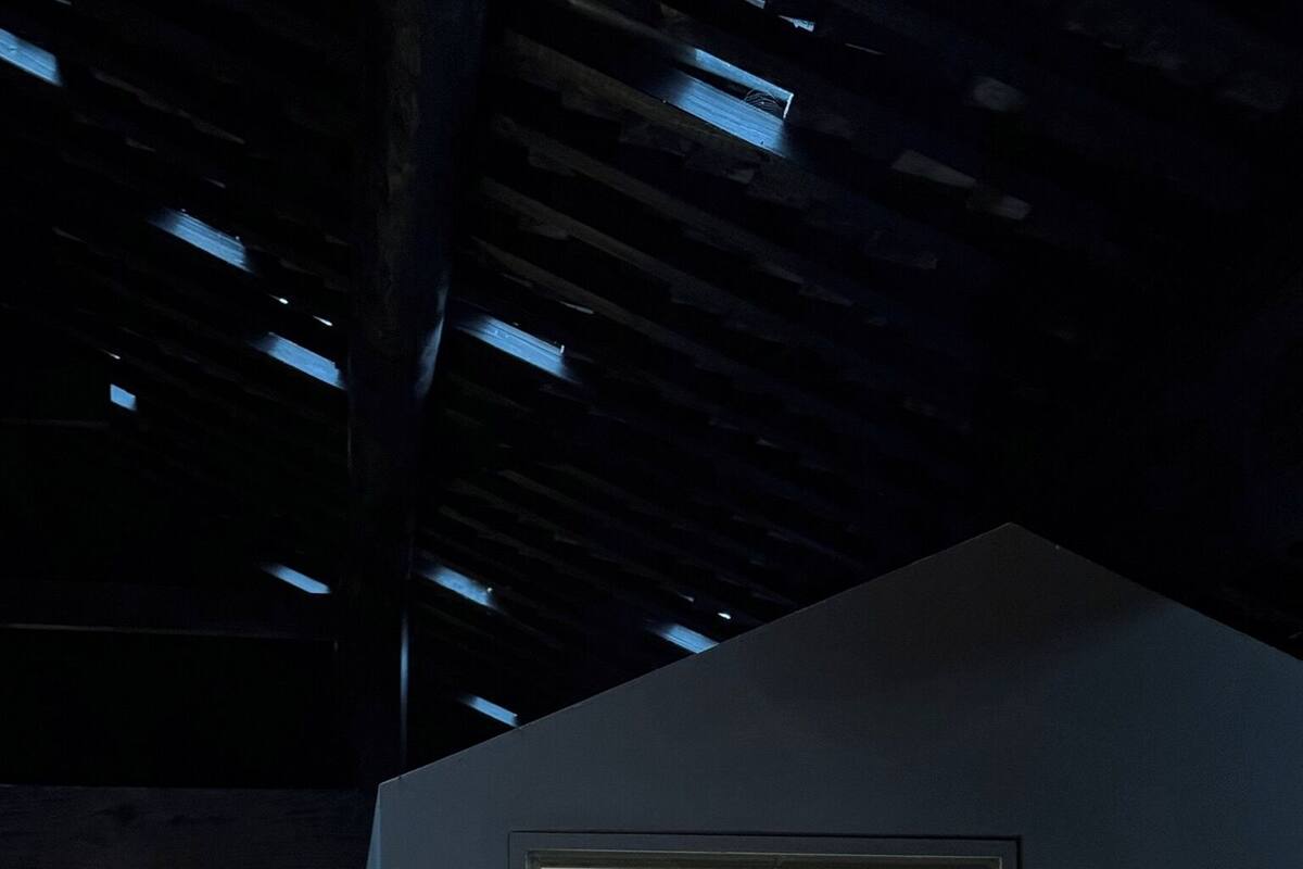 Une petite pièce sombre avec une fenêtre, des murs en bois et un plafond en pente.