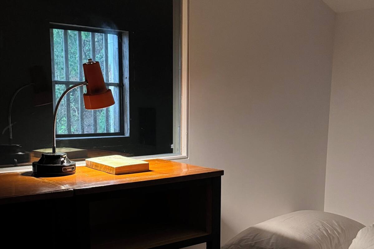 Une pièce avec un bureau, une lampe, une fenêtre et un lit.