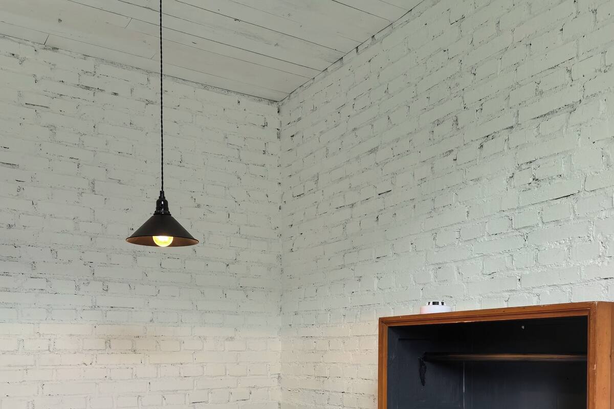 Un lit simple avec une literie blanche, un mur vert et une armoire en bois surmontée d’un plateau noir.
