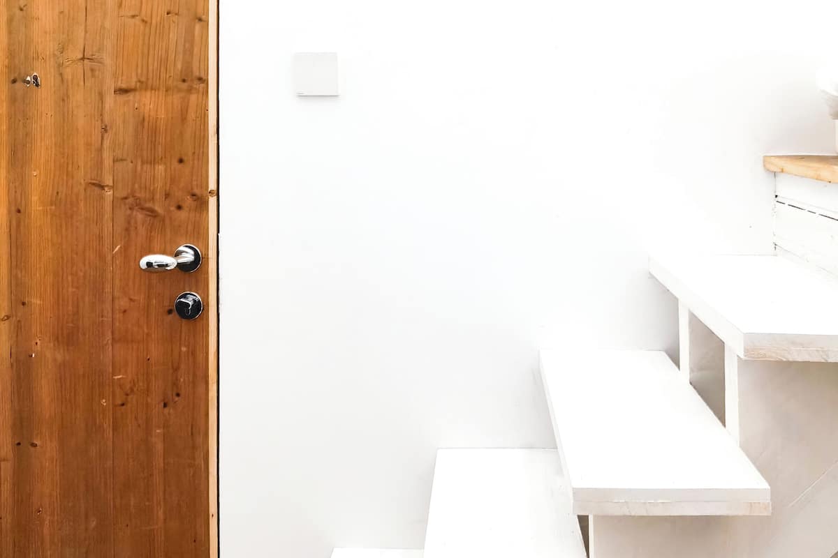Une porte en bois avec une poignée argentée et un mur blanc orné d’une sonnette blanche.