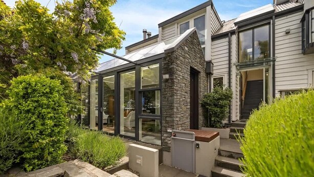 Une maison moderne dotée d’une véranda en verre, d’une façade en pierre et d’un jardin bien entretenu.