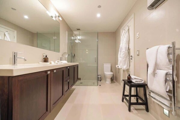 Un baño moderno con un espejo grande, cabina de ducha, inodoro y perchero para toallas.