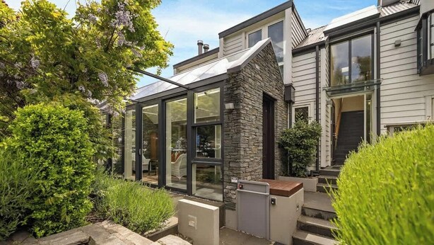 Une maison moderne dotée d’une véranda en verre, d’une façade en pierre et d’un jardin bien entretenu.