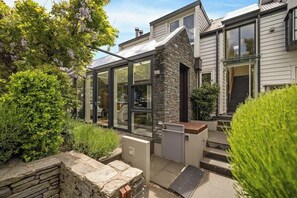 Une maison moderne dotée d’une véranda en verre, d’une façade en pierre et d’un jardin bien entretenu.
