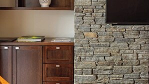 Un salon avec un mur en pierre, des étagères en bois, un téléviseur à écran plat et un canapé.