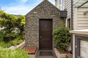 Un bâtiment revêtu de pierres, avec une porte marron foncé, un banc en bois et un jardin bien entretenu.