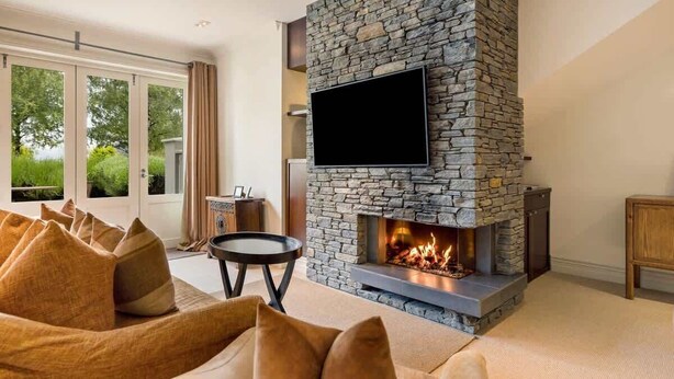 A living room with a stone fireplace, a flat-screen TV, and a sofa with cushions.