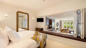 A bedroom with a large bed, a mirror, a television, and a view of a dining area through an open door.