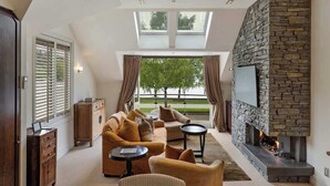 Una sala de estar moderna con chimenea de piedra, televisor de pantalla plana y un amplio ventanal con cortinas.