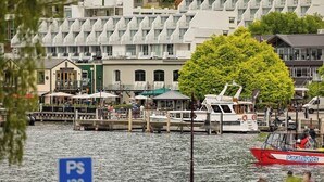 Zona costera con una hilera de edificios, un muelle con barcos y un letrero que indica la disponibilidad de estacionamiento.
