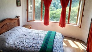 A bedroom with a bed, a ceiling fan, a window with red curtains, and a view of greenery outside.