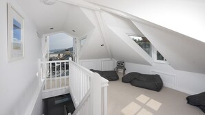 A spacious attic room with a sloped ceiling, a white staircase, and a view of the beach. - Salubrious Cottage -  a cottage that sleeps 6 guests  in 3 bedrooms (St Ives)