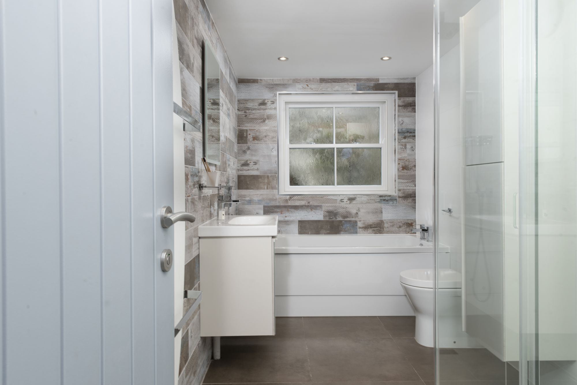 Un bagno moderno con box doccia in vetro, lavandino bianco e water.