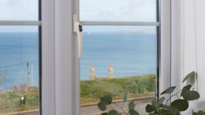 A view through a window of a coastal landscape with two stone structures, a road, and a body of water.