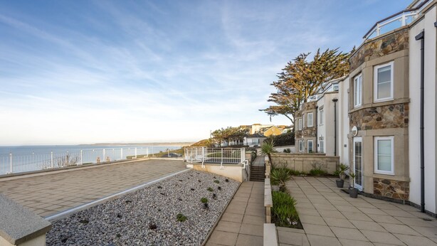 A coastal residential area with a paved walkway, a pebble garden, and stone buildings with multiple windows.