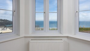 A room with three large windows overlooking a coastal view.