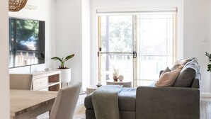 A modern living room with a grey sofa, a wooden dining table, and a TV mounted on the wall. - Austinmer On The Beach (Austinmer)