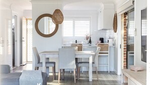 A modern kitchen with a dining area, featuring a round mirror, wicker chairs, and a light-colored dining table. - Austinmer On The Beach (Austinmer)