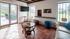 Un vaste espace de vie comprenant une table ronde en verre, un siège bleu rembourré, un canapé blanc et un téléviseur fixé au mur.