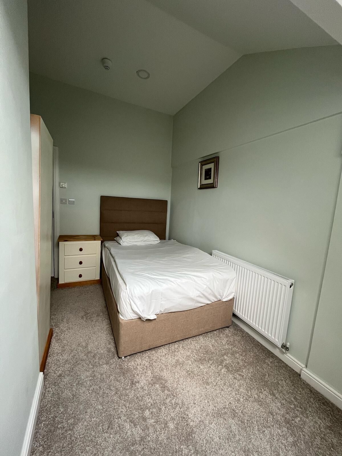 A bedroom with a bed, a nightstand, a dresser, and a radiator.