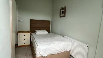 A bedroom with a bed, a nightstand, a dresser, and a radiator.