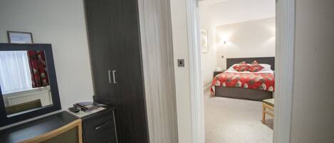 A bedroom with a bed, a bedside table, a dresser, and a mirror.