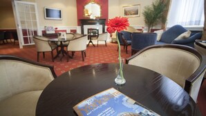 A hotel lobby with a round table, a red flower vase, a fireplace, and a television on the wall. - The White Swan Hotel (Halifax)