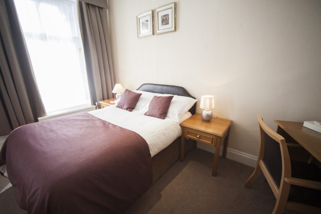 Ein Hotelzimmer mit Bett, Nachttisch, Schreibtisch und Stuhl.