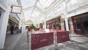 A covered walkway with glass ceiling, tables, and chairs set up for dining, and a sign for 'Por'tare No. 5 Westgate Arcade'. - The White Swan Hotel (Halifax)