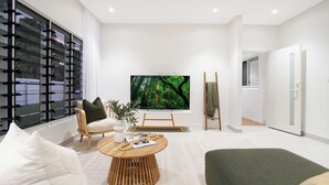Un soggiorno moderno con una grande TV, un tavolino di legno e un divano verde.