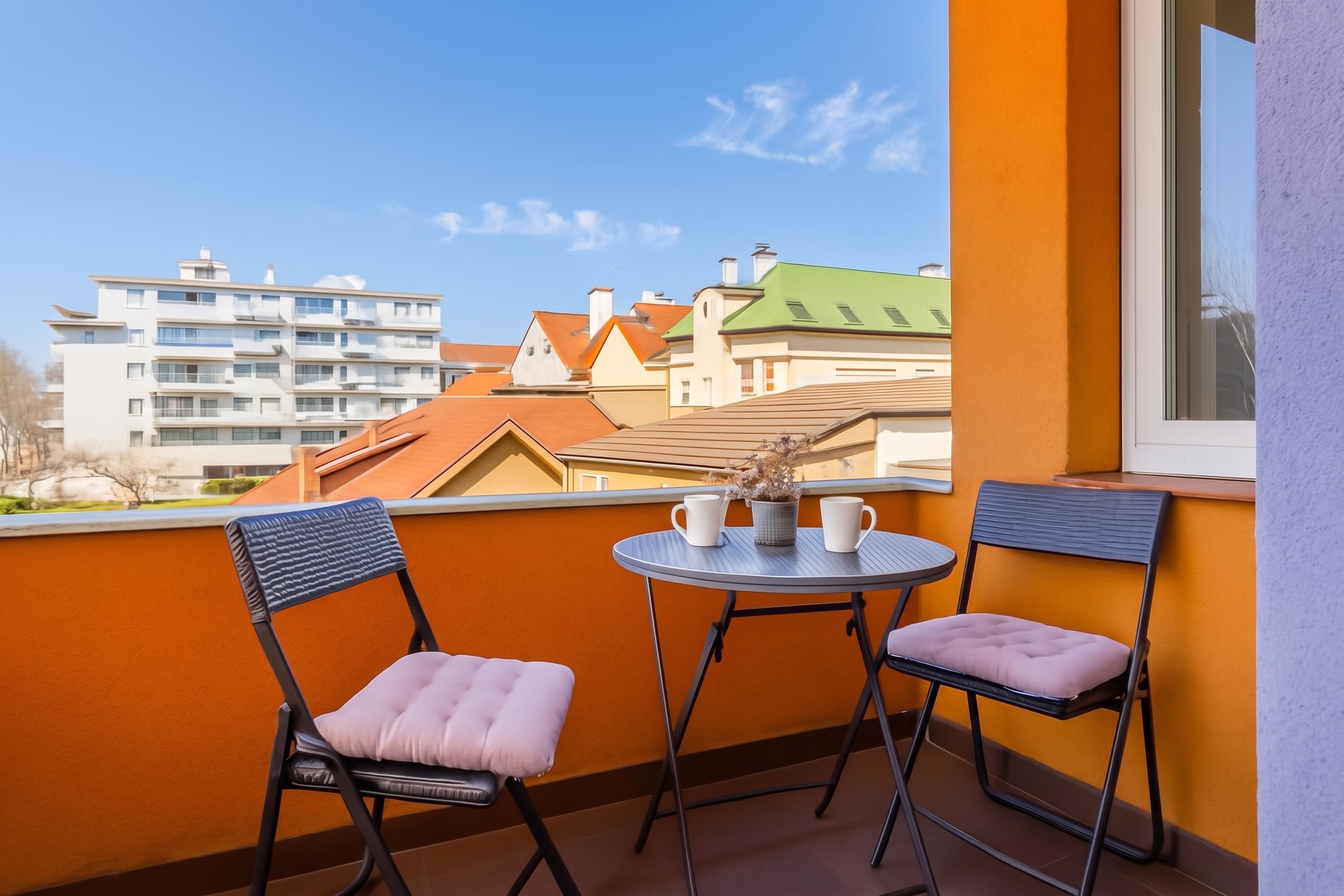 A balcony with two chairs and a small table, overlooking a residential area with various buildings.