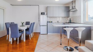 A modern kitchen with grey cabinets, a white refrigerator, and a microwave. There is a dining area with a white table and blue chairs. - Cherry City Stay Apartment With Parking (Zagreb)