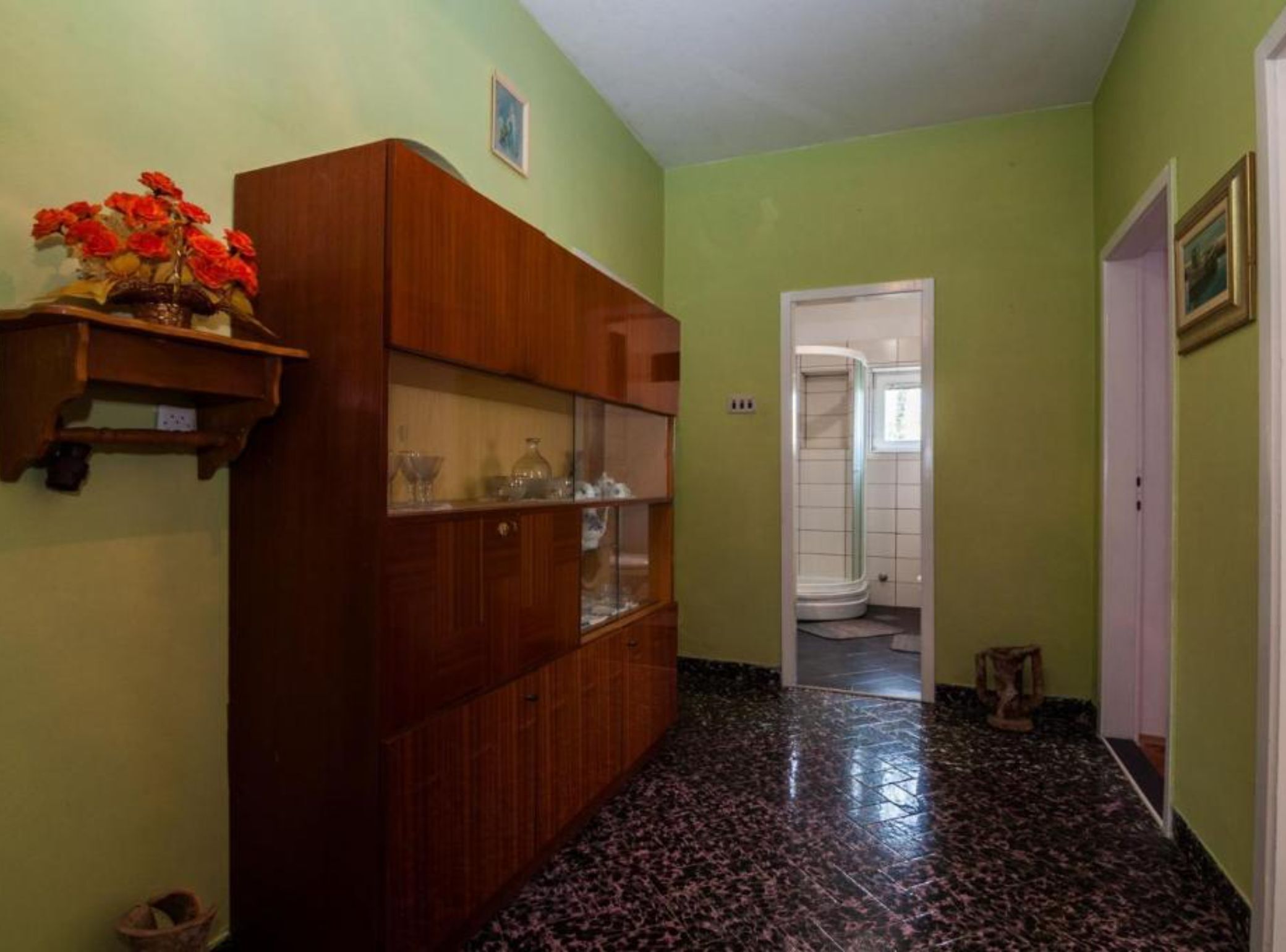 A hallway with a wooden cabinet, a tiled floor, and a door leading to a bathroom.
