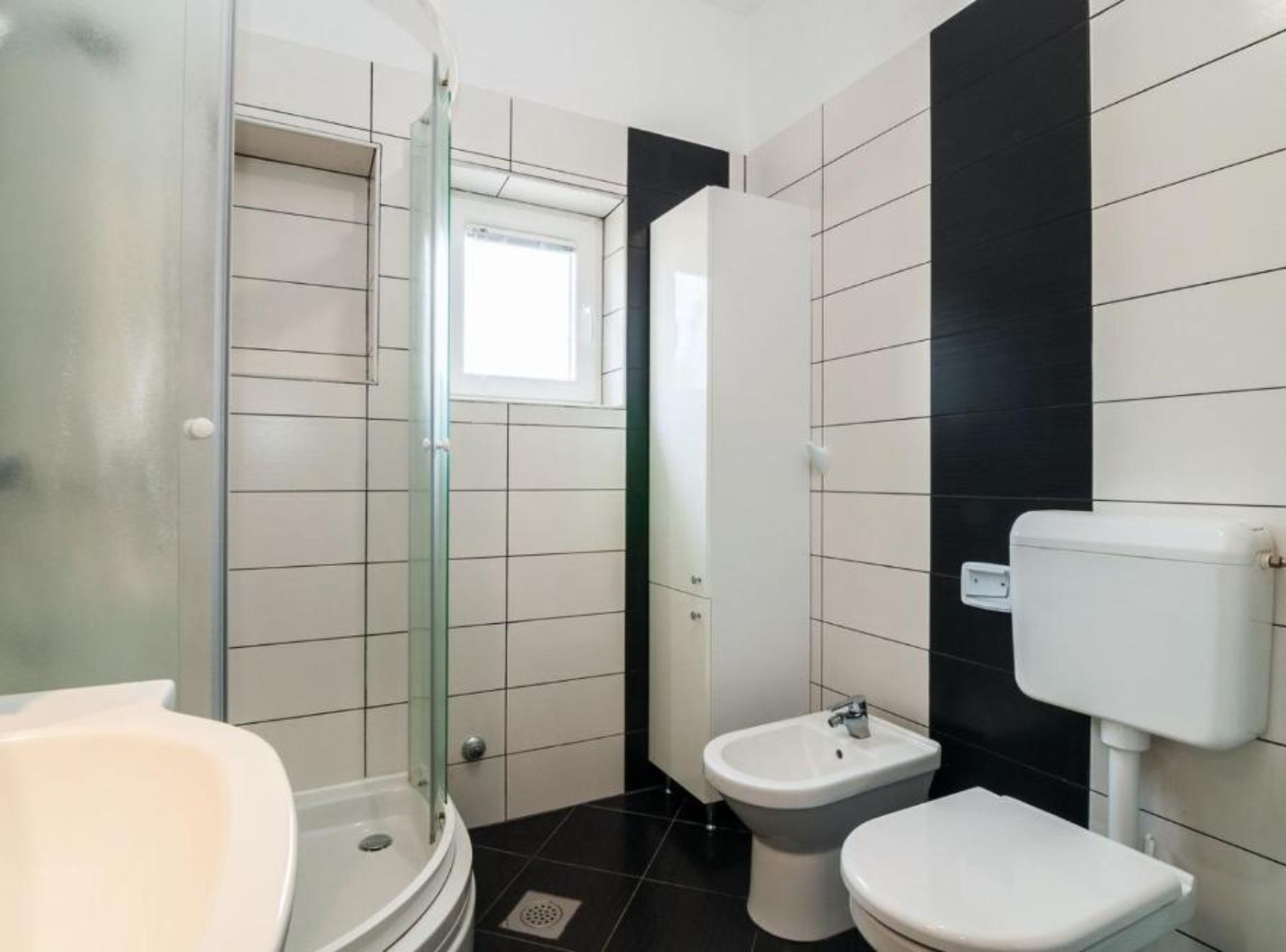 Een badkamer met een douche met glazen wand, een hygiëneschuiver, een toilet en een bad.