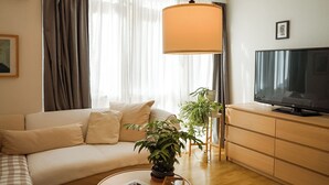 Un salon moderne avec un canapé, un téléviseur, une table basse agrémentée d’une plante et une grande fenêtre avec des rideaux.