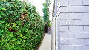 Une ruelle étroite, bordée d’un côté par une haie et de l’autre par un immeuble dont la façade porte le numéro 17.