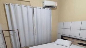 A hotel room with a bed, a window with white curtains, an air conditioning unit, and a wooden rack. - Hotel Líder (Caceres)
