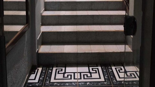 A staircase with a geometric patterned floor, a handrail on one side, and a metal railing on the other. - Hotel Líder (Caceres)